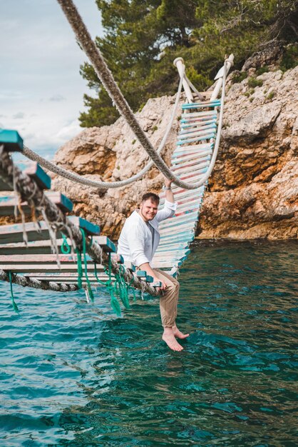 Hombre sentado en el puente colgante disfrutando de la vista al mar y la tranquilidad de la naturaleza