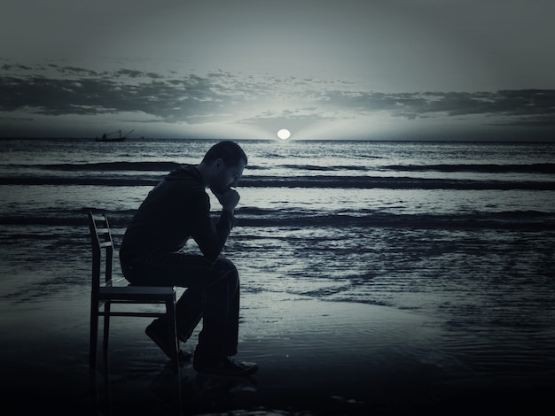 Foto hombre sentado en la silla en la costa por la noche