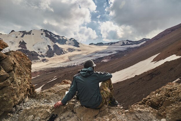 Hombre sentado sobre el campamento base del monte Kazbeg y disfrutando de la vista del glaciar Gergeti Meteostation en Kazbek Georgia Expedición alpinista del monte kazbek