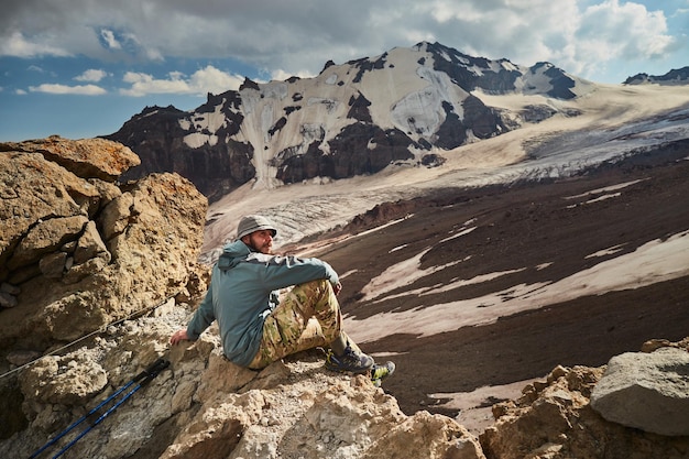 Hombre sentado sobre el campamento base del monte Kazbeg y disfrutando de la vista del glaciar Gergeti Meteostation en Kazbek Georgia Expedición alpinista del monte kazbek