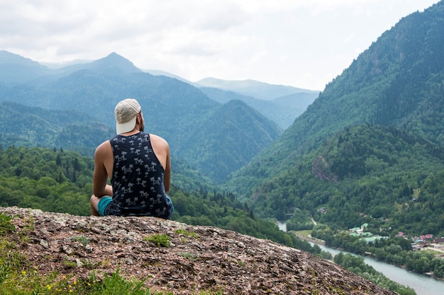 Hombre sentado sobre una roca y disfrutando de una hermosa vista del paisaje de montaña