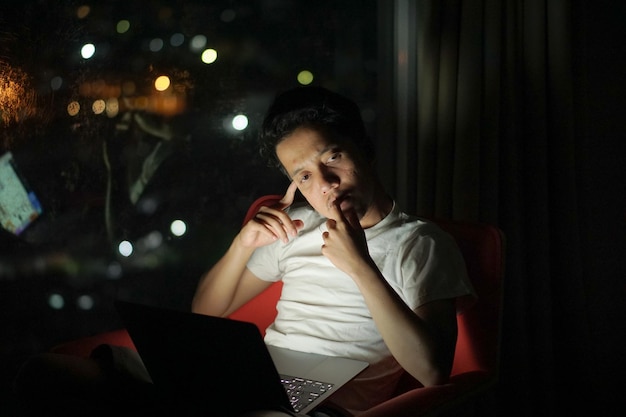 Foto un hombre está sentado en un sofá con una computadora portátil en la mano por la noche en el hotel