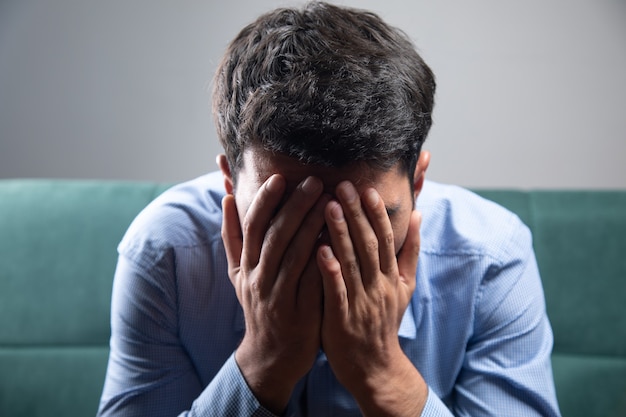 Un hombre sentado en el sofá que cubre su rostro.