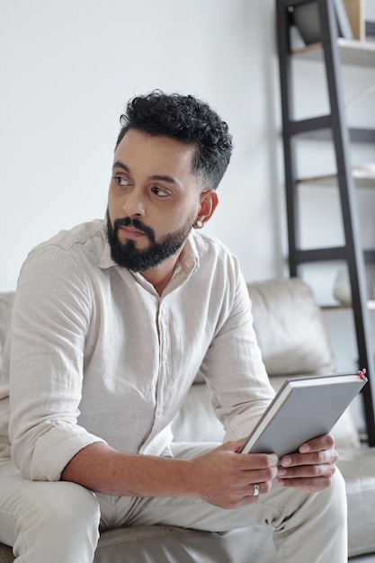 Hombre sentado en el sofá sosteniendo el diario de gratitud y mirando a otro lado