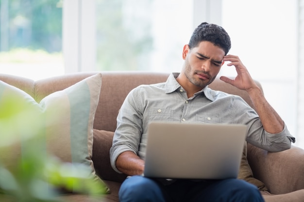 Hombre sentado en el sofá y usando una computadora portátil en la sala de estar en casa