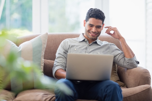 Hombre sentado en el sofá y usando una computadora portátil en la sala de estar