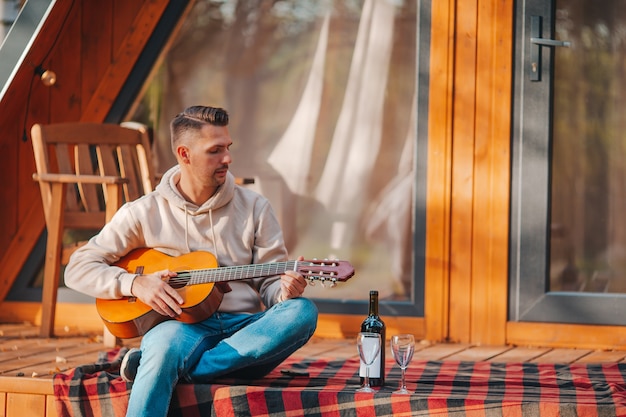 Hombre sentado en la terraza de su casa en otoño tocando la guitarra