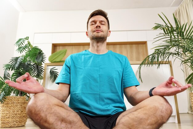 Un hombre sereno medita en posición de loto evocando paz y atención en medio de la vegetación interior con los ojos cerrados en contemplación