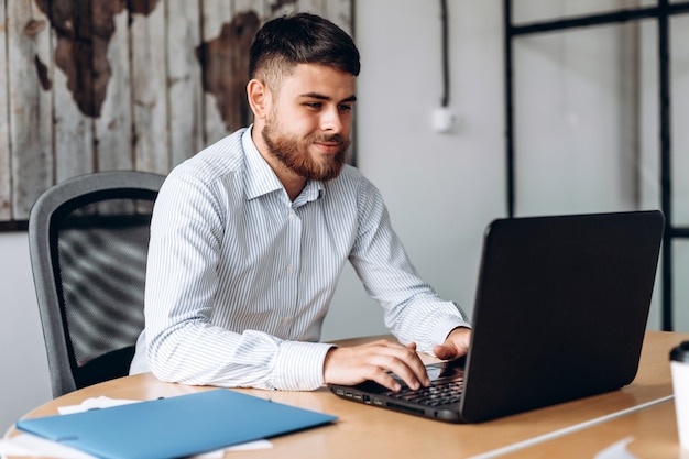 Foto hombre serio y barbudo trabajando en una computadora en la oficina