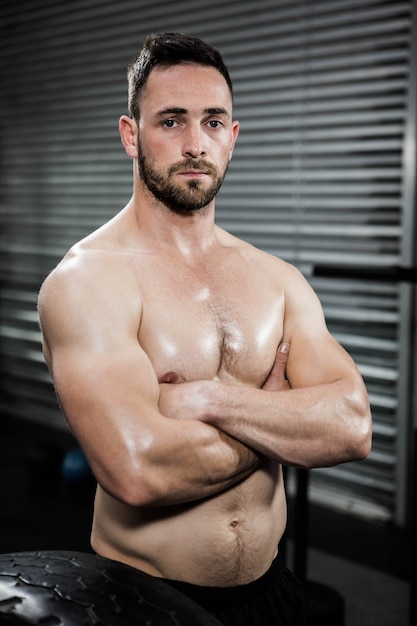 Hombre serio sin camisa con los brazos cruzados en el gimnasio de crossfit