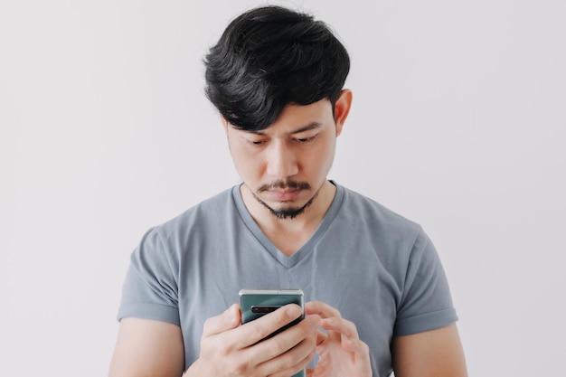 Hombre serio en camiseta azul usa smartphone aislado sobre fondo blanco.