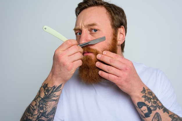 Hombre serio con cuchilla se centra en cortarse la barba