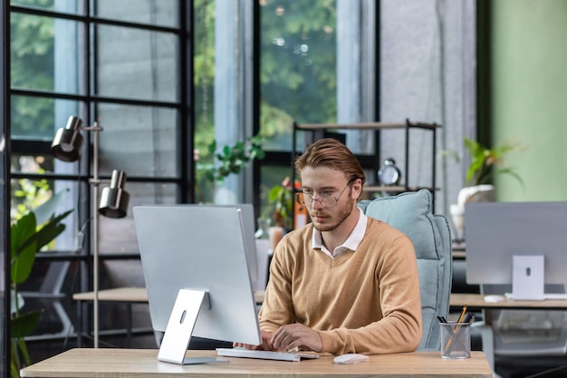 Hombre serio y desdeñoso en la oficina en el trabajo con un hombre de computadora escribiendo cuidadosamente en