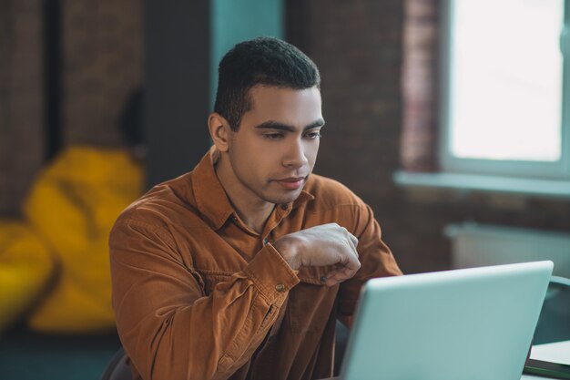 Hombre serio inteligente mirando la pantalla de la computadora mientras piensa en su trabajo