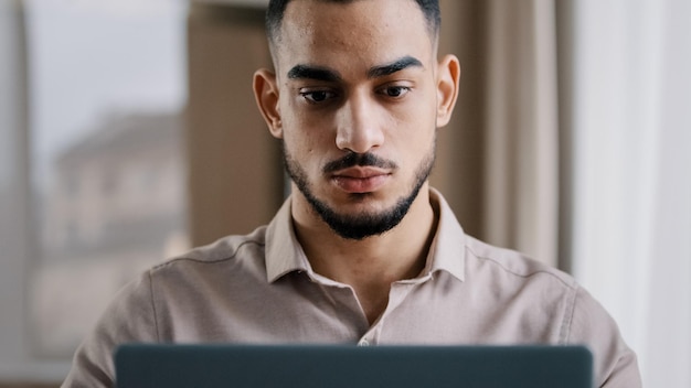 Hombre serio joven hombre de negocios hispano inversionista agente independiente escribiendo en la computadora en la oficina en casa