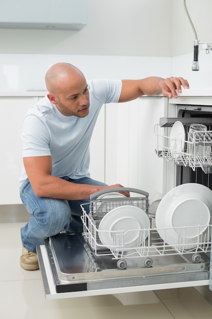 Foto hombre serio con lavavajillas en la cocina