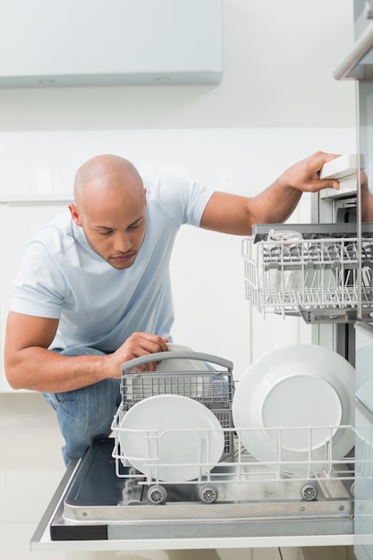 Foto hombre serio con lavavajillas en la cocina