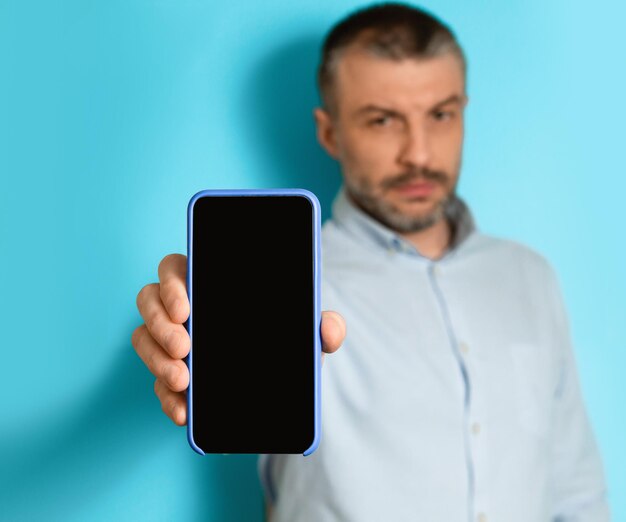 Hombre serio de mediana edad que muestra el fondo azul de la pantalla en blanco del teléfono