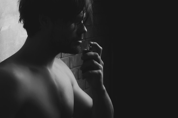 Hombre sexy con el pecho desnudo oliendo aroma de perfume
