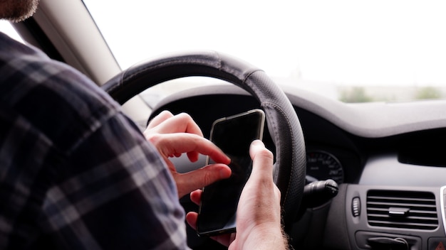 Un hombre se sienta en un automóvil con un teléfono móvil en la mano y escribe mensajes de texto mientras conduce