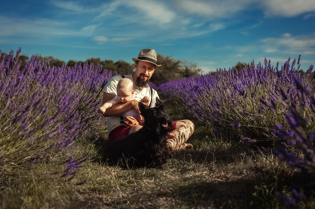 Un hombre se sienta en un campo de lavanda con un bebé y un perro.