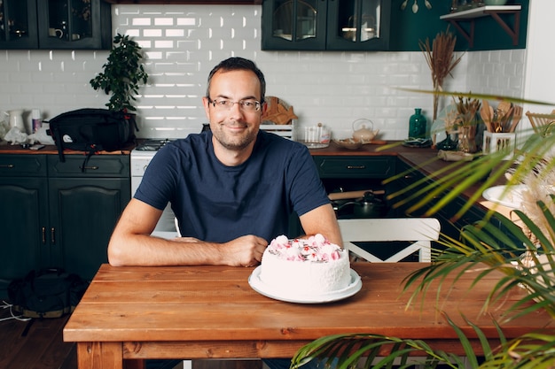 El hombre se sienta en la cocina de casa con pastel en la mesa.