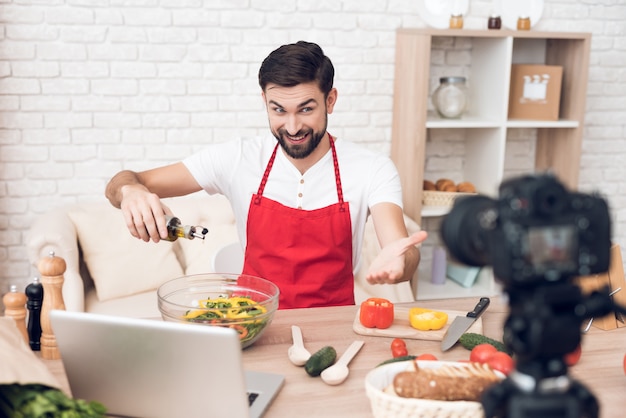 Un hombre se sienta en un delantal y cocina ante la cámara.