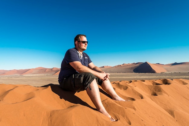 Un hombre se sienta en una duna de arena en el desierto de namib