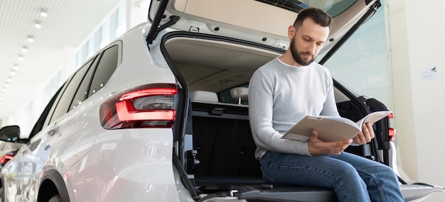 Un hombre se sienta en el maletero de un coche mirando una oferta de seguros