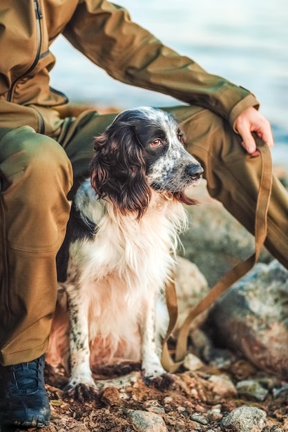 Un hombre se sienta en la orilla del río con su perro de caza spaniel