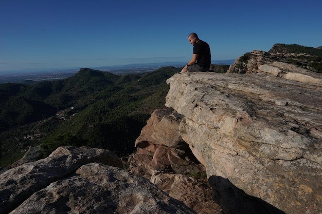 Un hombre se sienta en una roca con vistas a las montañas.