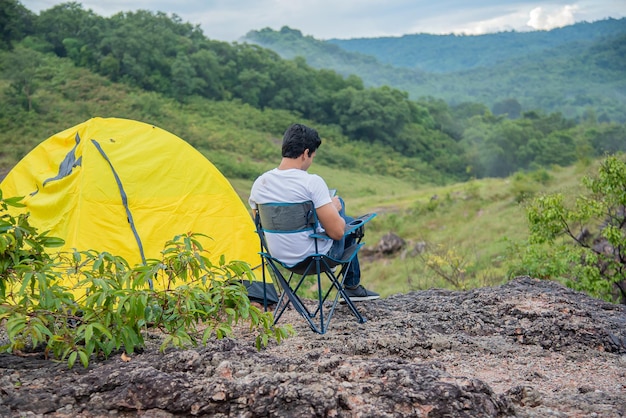 El hombre se sienta en una silla relajándose entre las hermosas montañas con una carpa a su lado