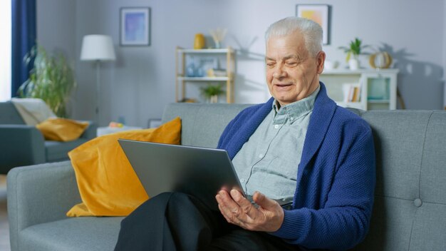 Un hombre se sienta en un sofá con una computadora portátil en la mano.