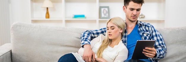 El hombre se sienta con una tableta cerca de la mujer dormida.