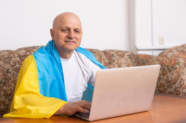 El hombre se sienta en un trabajo con una computadora portátil y una bandera de Ucrania