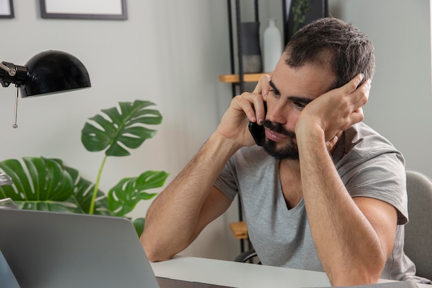 El hombre se siente cansado mientras trabaja desde casa y habla por teléfono