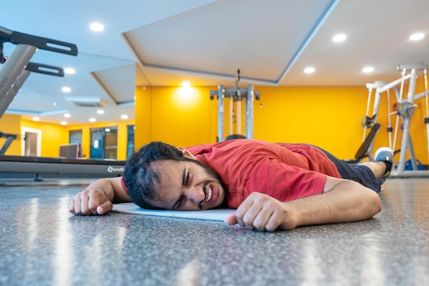 el hombre siente dolor muscular después del entrenamiento mientras está acostado en el piso del GIMNASIO