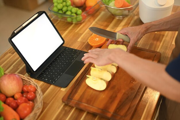 Hombre siguiendo una receta en línea en una tableta digital mientras hace una comida saludable en una cocina