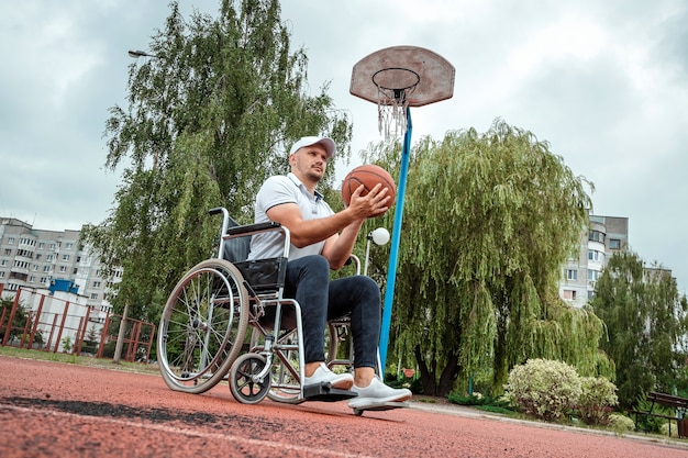 Un hombre en silla de ruedas juega baloncesto en el campo de deportes. El concepto de una persona discapacitada, una vida plena, una persona con una discapacidad, fitness, actividad, alegría.