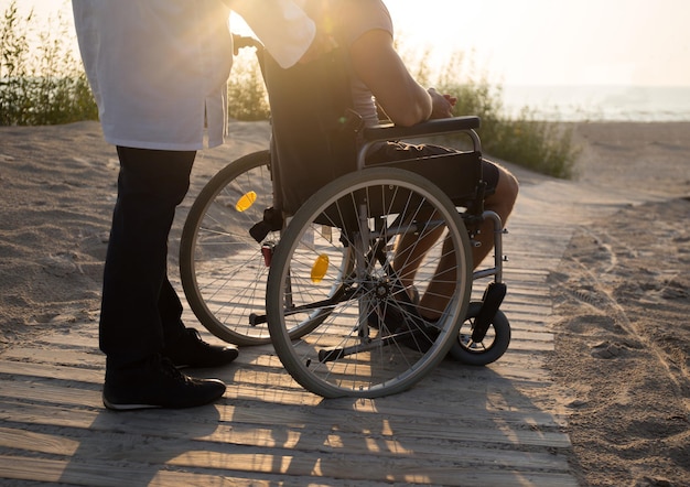 Hombre en silla de ruedas y médico en la playa.