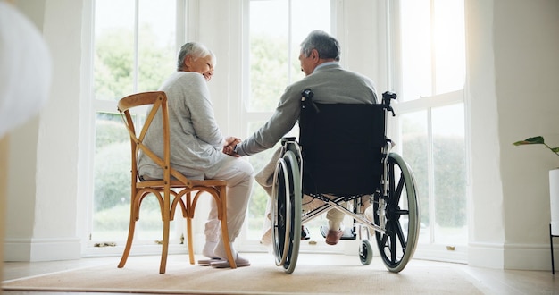 Hombre en silla de ruedas y mujer conforto en el hogar para la relación unión amor confianza o ayuda mano esposa y marido con una discapacidad juntos por la mañana o jubilación relajarse cuidado compasión o apoyo