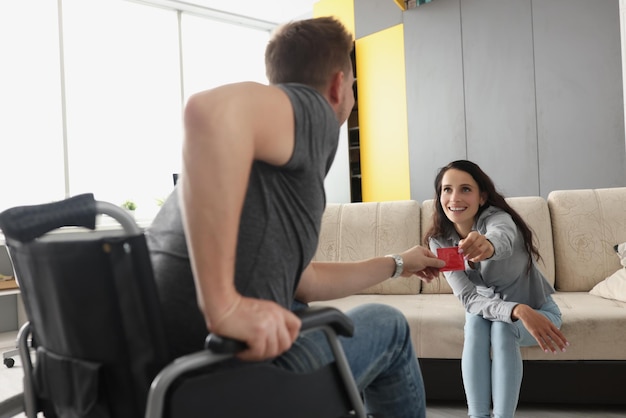 Hombre en silla de ruedas toma condón de esposa sonriente sentarse en sofá pareja feliz celebrar potencia