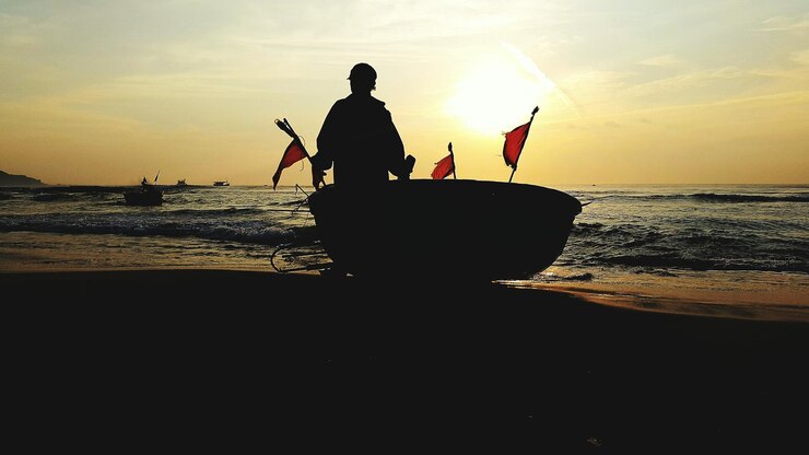 Foto hombre silueta con barco en la playa contra el cielo durante la puesta de sol