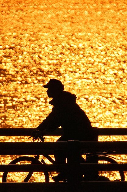 Hombre silueta en bicicleta en el puente sobre el mar durante la puesta de sol