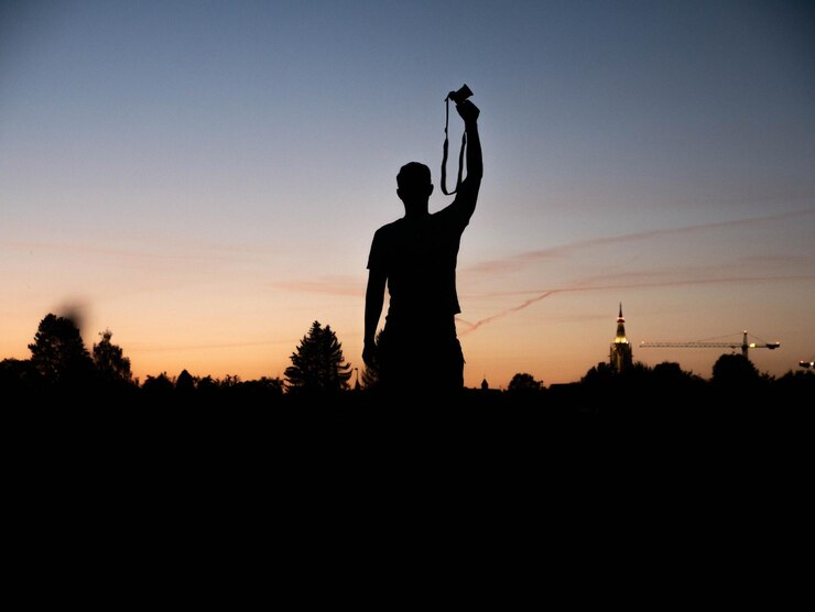 Foto hombre silueta con cámara de pie contra el cielo durante la puesta de sol