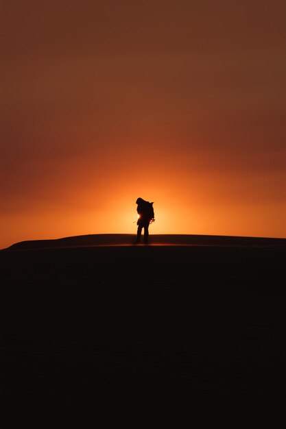 Foto hombre silueta caminando por el campo contra el cielo naranja