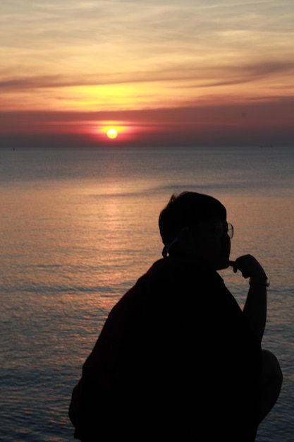 Foto hombre silueta mirando al mar contra el cielo durante la puesta de sol