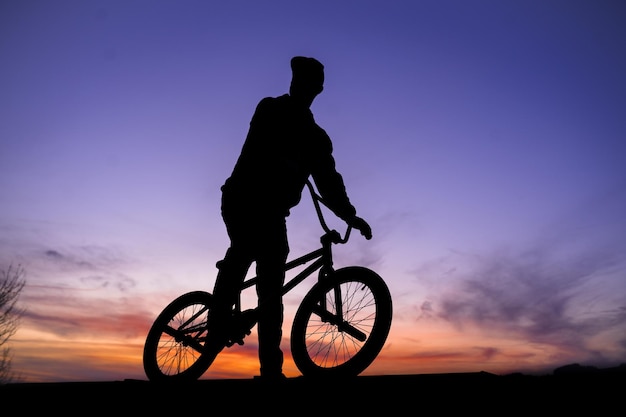 Foto hombre silueta montando en bicicleta contra el cielo durante la puesta de sol