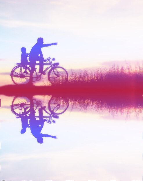 Hombre silueta montando en bicicleta por el lago contra el cielo durante la puesta de sol