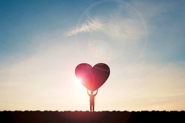 El hombre de la silueta muestra dos manos levantadas y llevando el corazón con la luz del sol y el cielo azul, concepto del día de San Valentín.